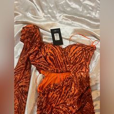 an orange dress with sequins on it laying on a white sheeted bed