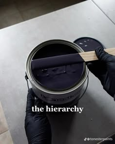 a person in black gloves holding a paint can with the words the hierarchy on it