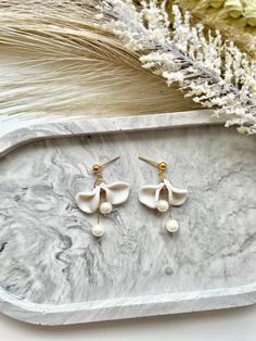 two white flower shaped earrings on a marble tray