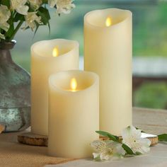 three lit candles sitting on top of a table next to a vase filled with flowers