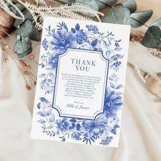 a blue and white thank you card with flowers on it next to some dried leaves