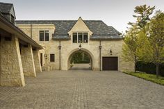 a large brick driveway leading to a house with an arched doorway and stone walkway between two buildings