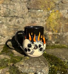 a black and white coffee cup with flames painted on it's side sitting on some rocks