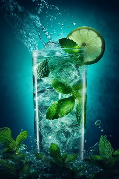 a glass filled with ice and lime slices on top of water surrounded by mint leaves