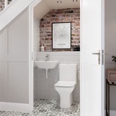 a white toilet sitting next to a bathroom sink under a stair case in a brick wall