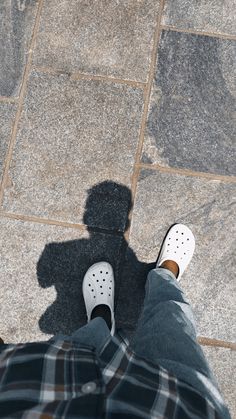 the shadow of a person's feet and shoes on a tile floor with a black and white checkered shirt