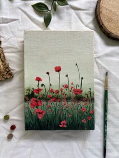 a painting of red poppies on a white sheet next to a green brush and some other items