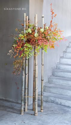 three tall bamboo poles with flowers in them on the side of a building next to some stairs