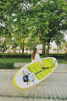 a woman holding a surfboard on top of a brick walkway in front of trees