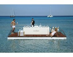 two people standing on a floating bar in the ocean