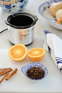 an orange cut in half next to some cinnamon sticks and a crock pot on a table