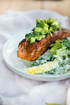 a white plate topped with meat covered in green veggies on top of a table