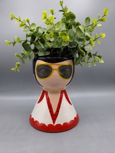 a ceramic vase with a plant in it and sunglasses on the top, sitting on a table