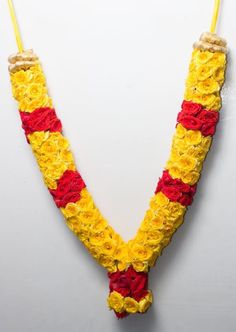 a yellow and red flowered necklace hanging from a hook on a white wall in the shape of a letter v