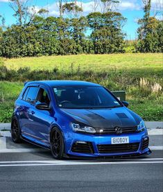 a blue vw golf gtr is parked on the side of the road in front of some trees