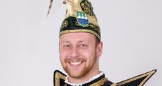 a man wearing a crown and standing in front of a white wall