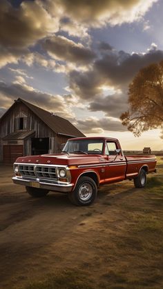 an old red pickup truck parked in front of a barn with a tree on the side