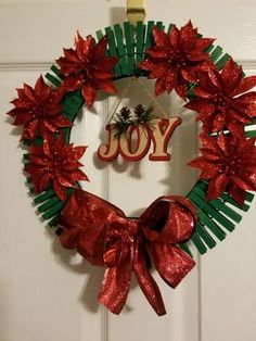 a red and green christmas wreath hanging on a door with the word joy written in it