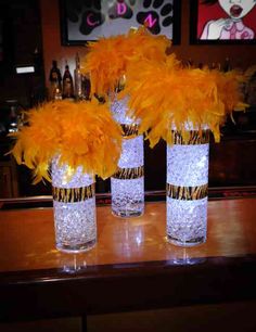 three clear vases with yellow feathers on a table in front of a bar top