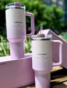 two pink tumblers sitting on top of a wooden table next to a planter