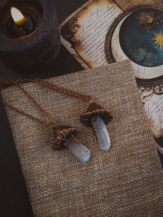 two necklaces sitting on top of a piece of paper next to a lit candle