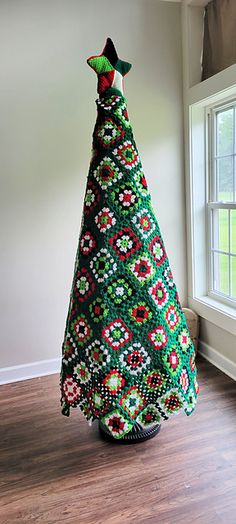 a crocheted christmas tree sitting on top of a wooden floor next to a window