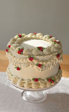 a cake with white frosting and red flowers on it sitting on a glass plate