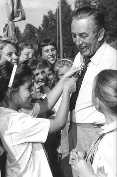 an old black and white photo of a group of people with one man helping another woman put on her tie