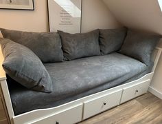 a gray couch sitting under a window on top of a wooden floor next to drawers