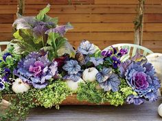 a basket filled with purple flowers sitting on top of a wooden table next to pumpkins