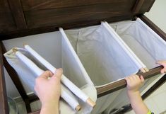 a person holding two rolls of toilet paper in front of a wooden cabinet with white liners