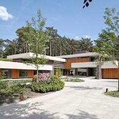 a modern house surrounded by trees and flowers in the foreground is an empty driveway