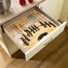 an open drawer with knives and spoons in it on a wooden floor next to a counter