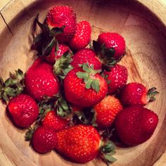 a wooden bowl filled with lots of ripe strawberries