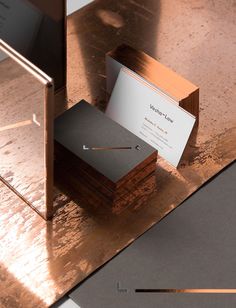 two business cards sitting on top of a wooden table next to a metal box with a card in it