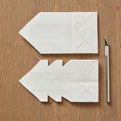 two pieces of paper with an origami arrow cut out next to a pen