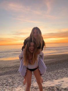 two young women standing on the beach with their arms around each other as the sun sets