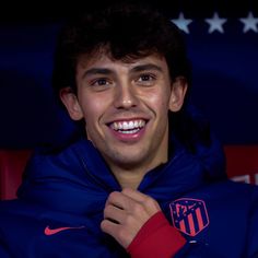 a young man in a blue jacket smiles at the camera while wearing a red and white nike hoodie