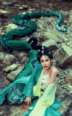 a woman sitting on the ground next to a snake