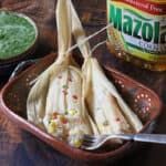 two tamales with corn and salsa in a bowl next to a jar of mayonnaise