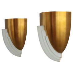 two gold and white wall sconces with curved edges on each side, set against a white background