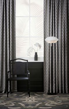 a black chair sitting in front of a window next to a white vase with flowers