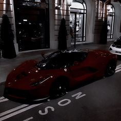 a red sports car parked in front of a building at night with two other cars behind it