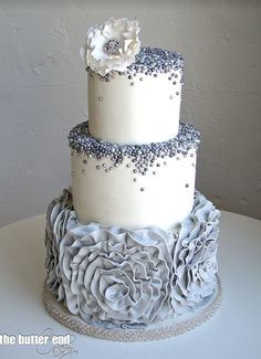 a three tiered wedding cake with white and gray frosting flowers on the top