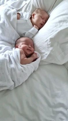 two babies are sleeping in white blankets on a bed