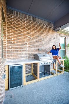 a woman sitting on top of an outdoor bbq grill next to a brick wall