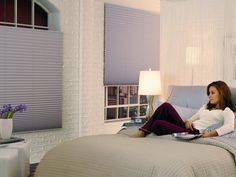 a woman sitting on top of a bed in a room with white walls and windows