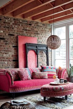 a living room with red couches and colorful pillows on the floor next to a brick wall