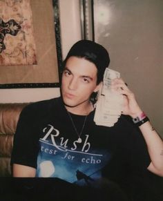 a young man sitting on a couch holding a remote control to his ear and looking at the camera