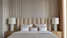 a large bed with white pillows and beige headboard